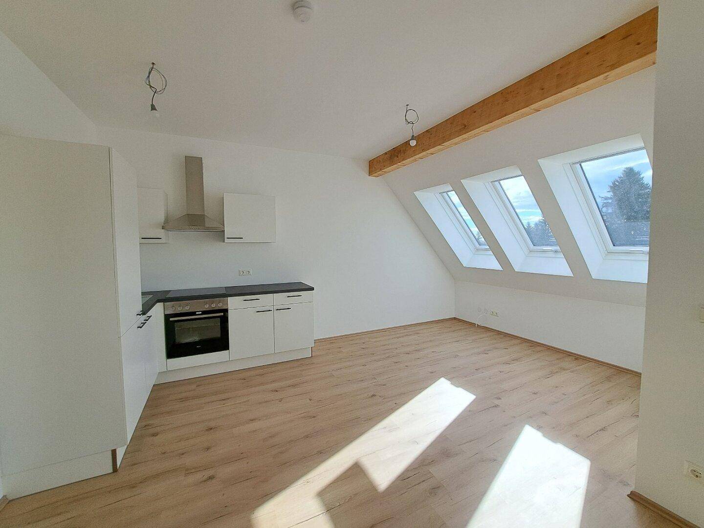 Offener Wohnbereich mit Küchenzeile, Holzbalken und schrägen Dachfenstern für viel Licht.