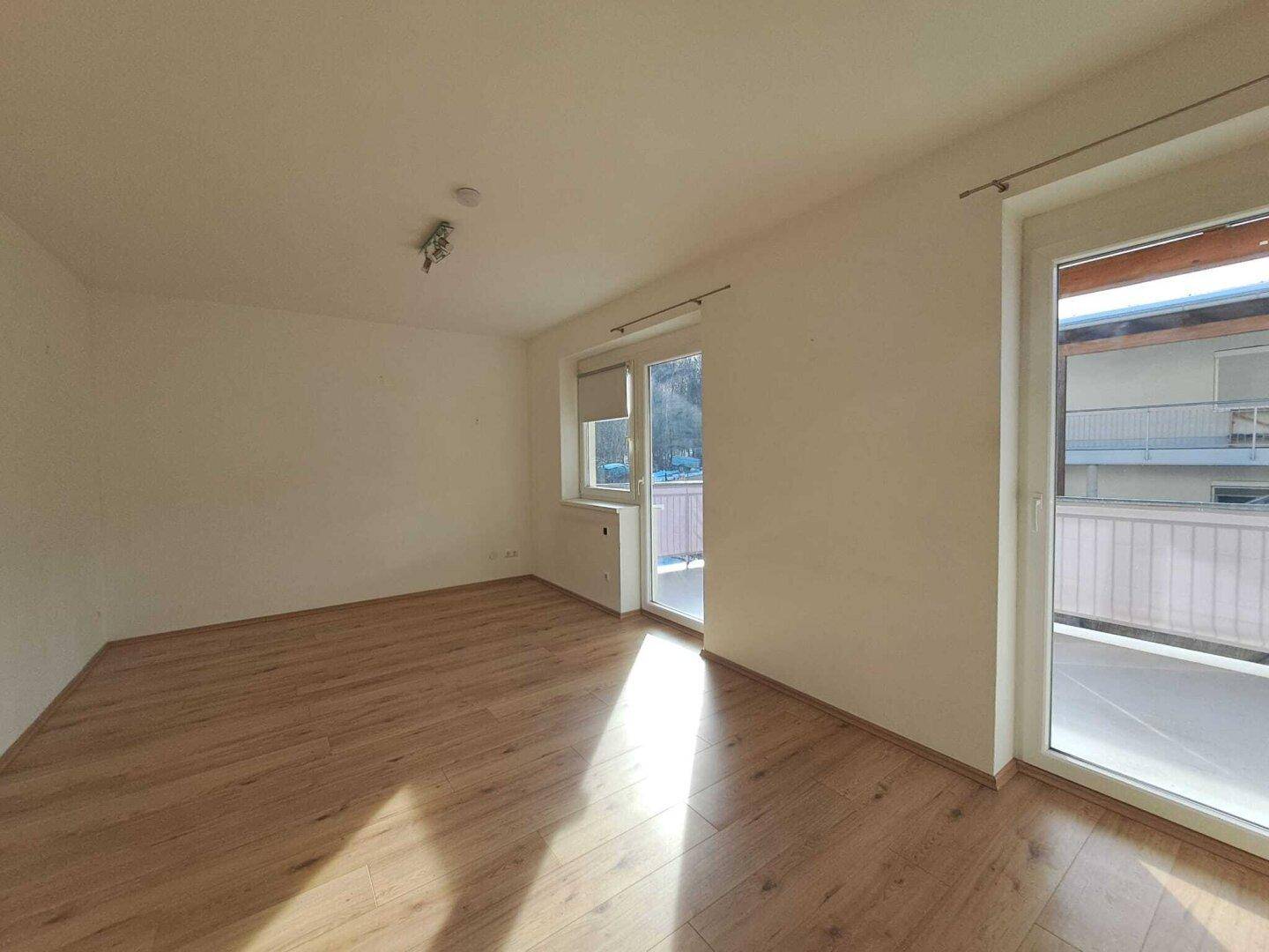 Helles Wohnzimmer mit Holzboden und großzügigem Zugang zum Balkon.