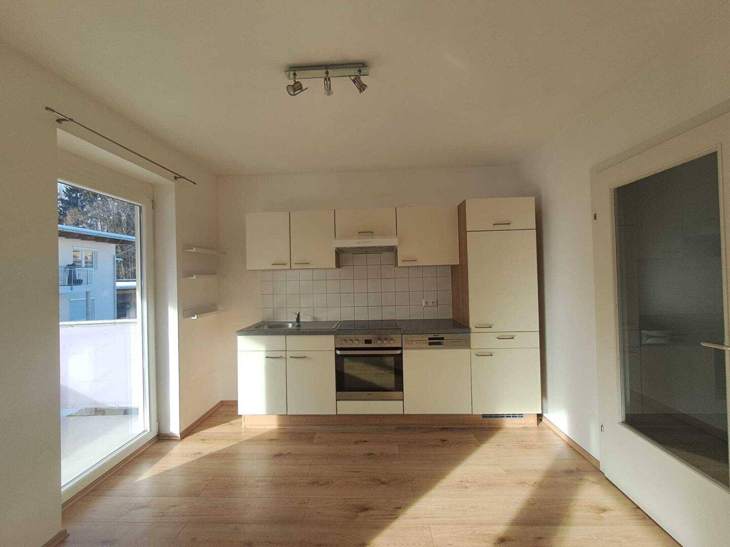 Helle Küche mit Einbauküche, Holzboden und Zugang zum Balkon.