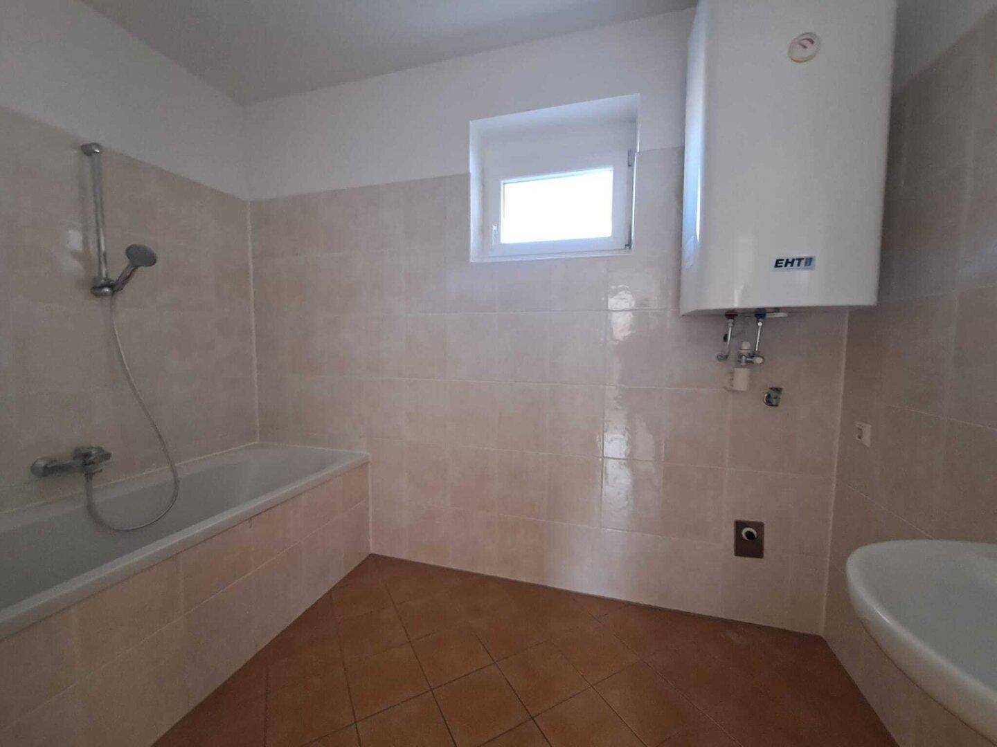 Badezimmer mit Badewanne, Fenster und Warmwasserboiler an der Wand.