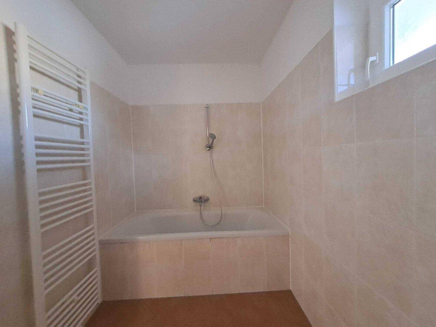 Badezimmer mit Badewanne, beigefarbenen Fliesen und beheiztem Handtuchhalter.