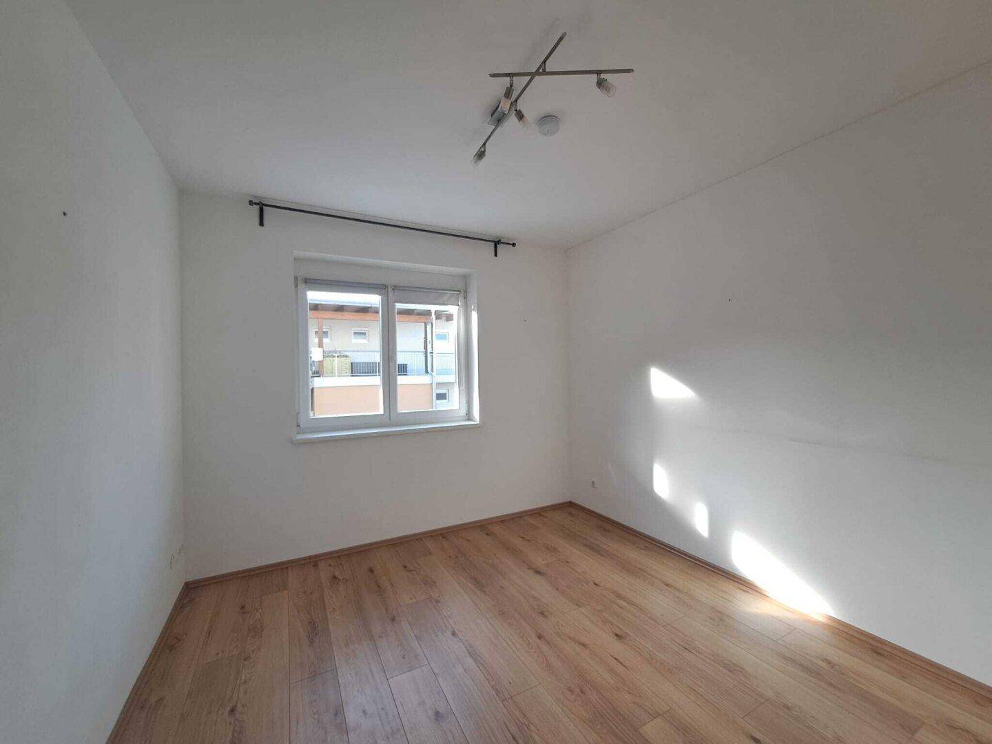 Leeres Zimmer mit Holzboden und großem Fenster, ideal als Schlafzimmer.