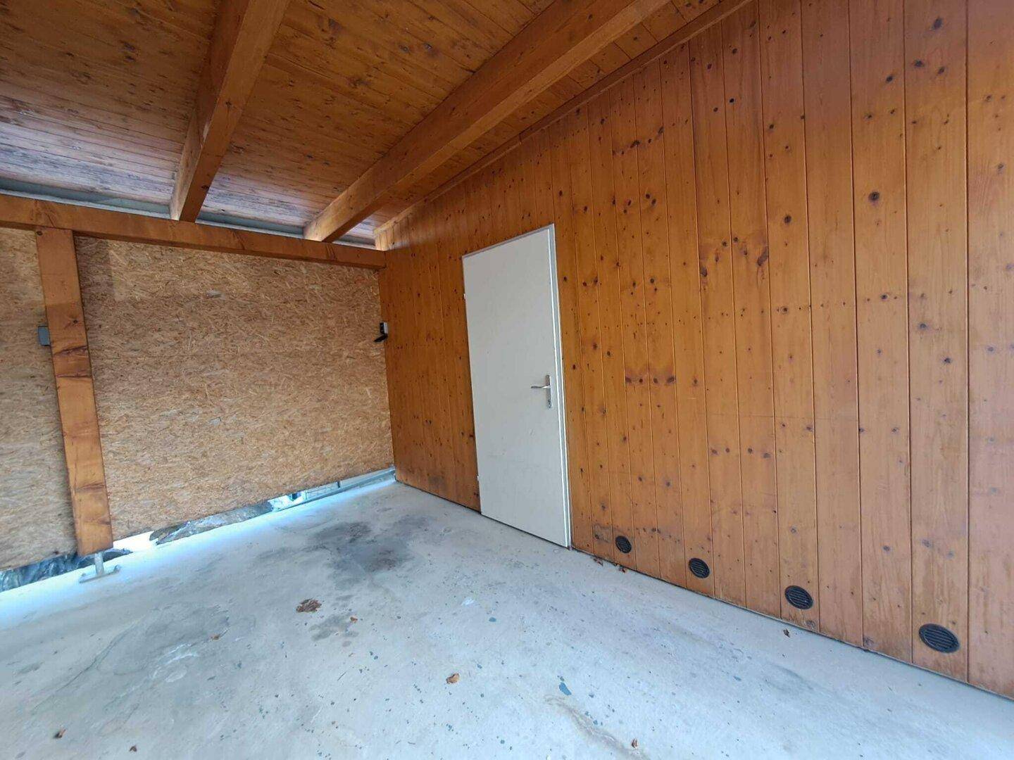 Innenansicht eines Holzschuppens mit einfacher Tür und Holzverkleidung.