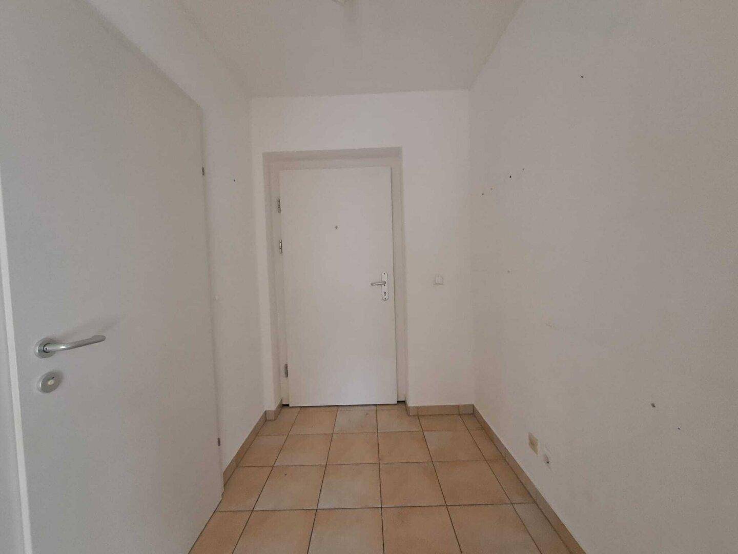 Heller Flur mit Fliesenboden und weiß gestrichenen Wänden.