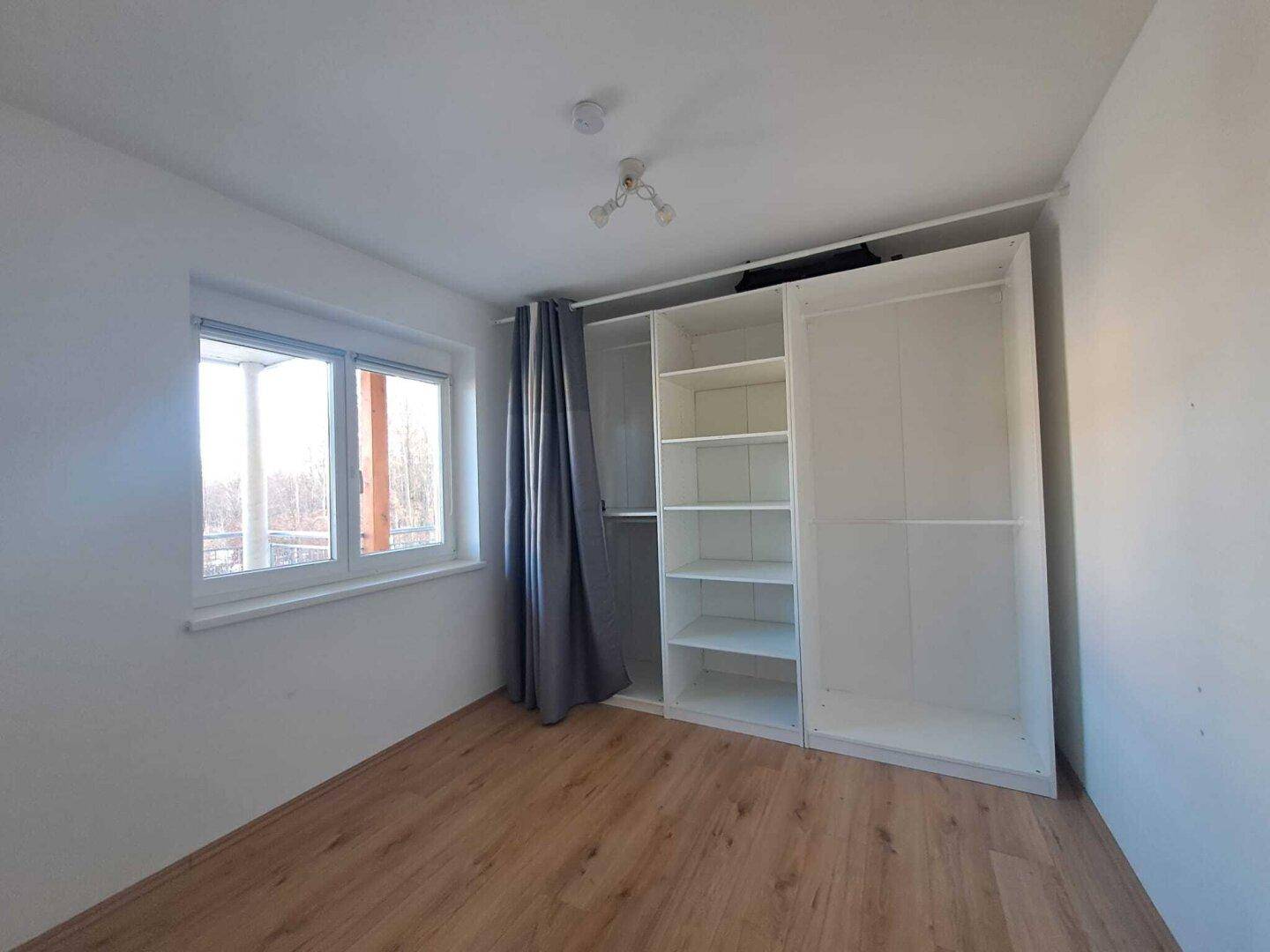 Schlafzimmer mit Holzboden, Fenster und offenem Kleiderschrank.