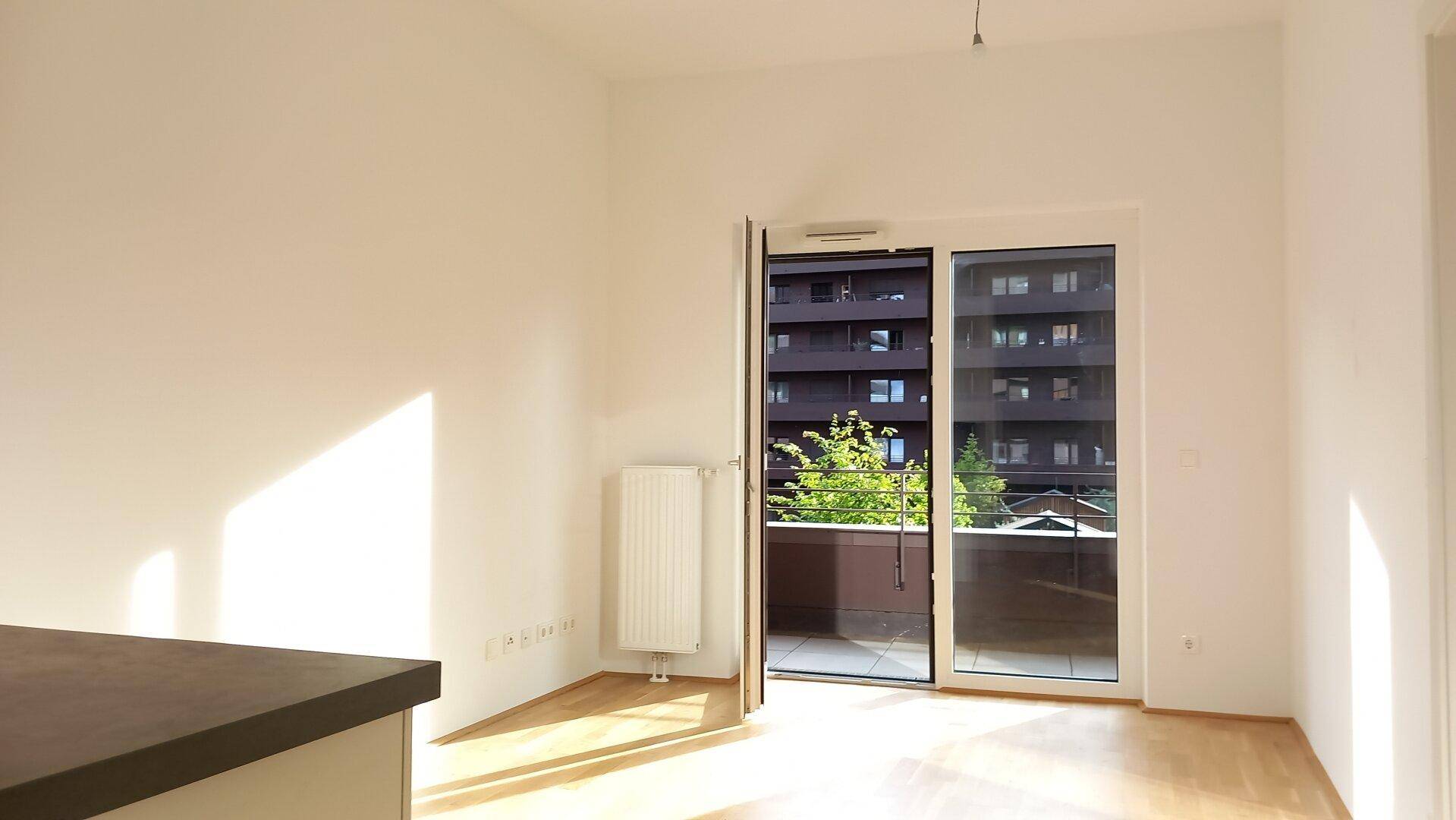 Heller Wohnbereich mit Holzboden und Zugang zu einem Balkon mit Blick auf moderne Gebäude.