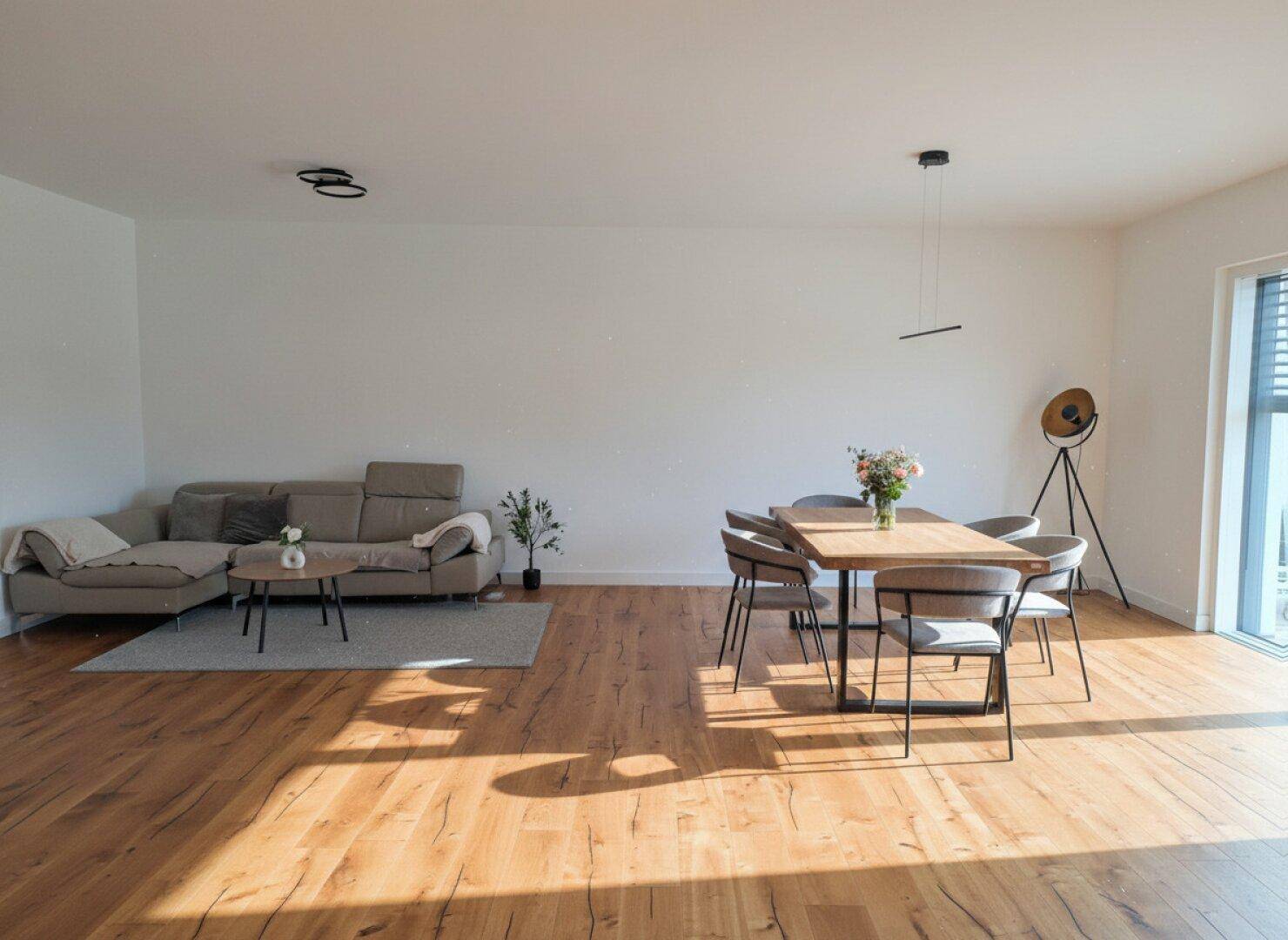 Heller Wohn- und Essbereich mit bequemer Couch, Holzboden und viel Tageslicht.