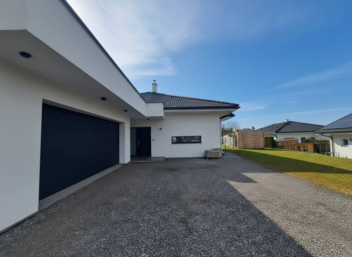 Seitenansicht des Hauses mit Garage, Kiesauffahrt und gepflegtem grünem Rasen.