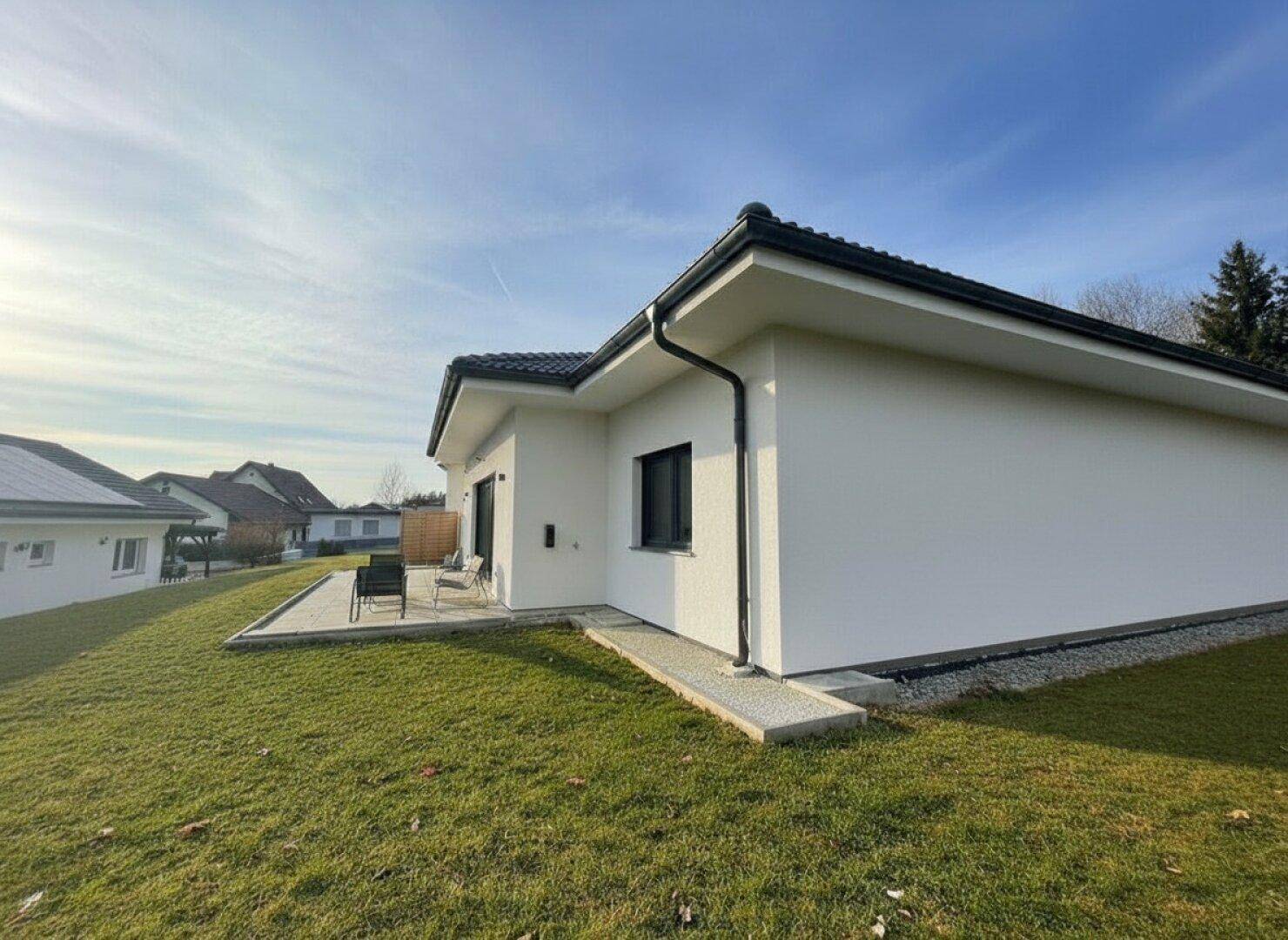 Seitenansicht des modernen Hauses mit Rasenfläche und Blick zur Terrasse im Hintergrund.