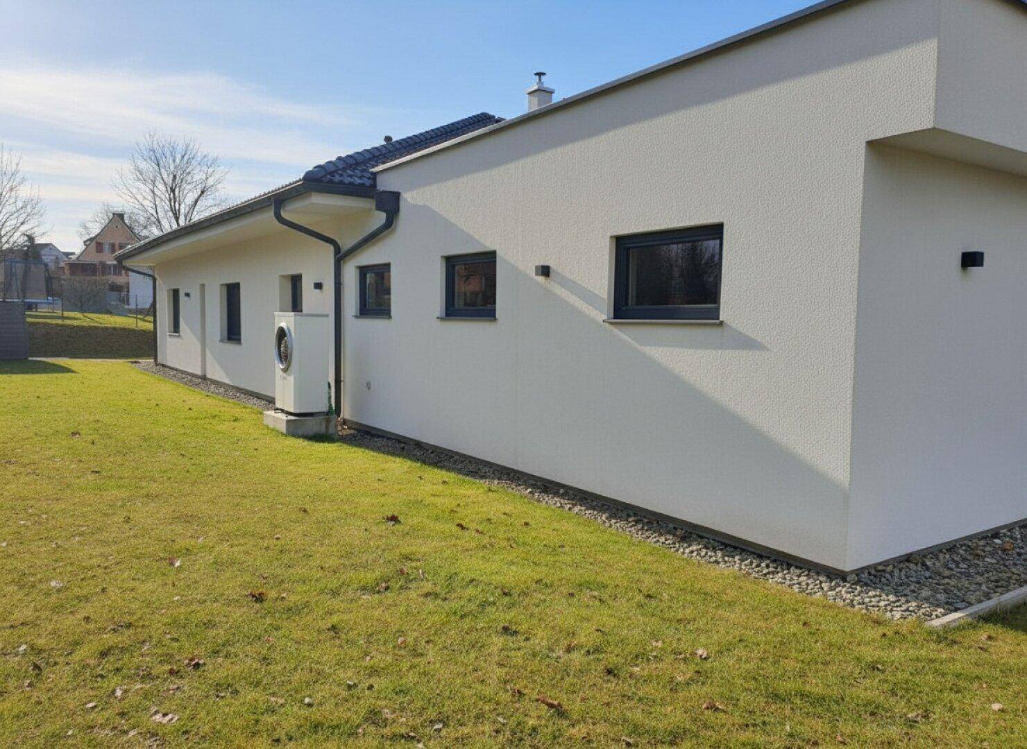 Seitenansicht des Hauses mit einer sichtbaren Wärmepumpe und grünem Rasen.