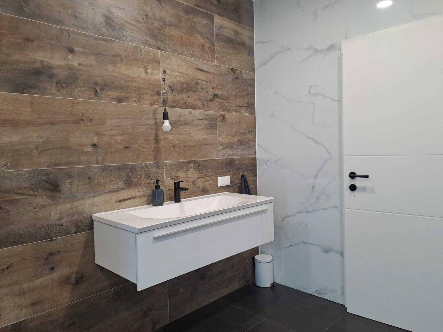 Modernes Badezimmer mit schwebendem Waschtisch, Holzoptik-Fliesen und weißer Tür.