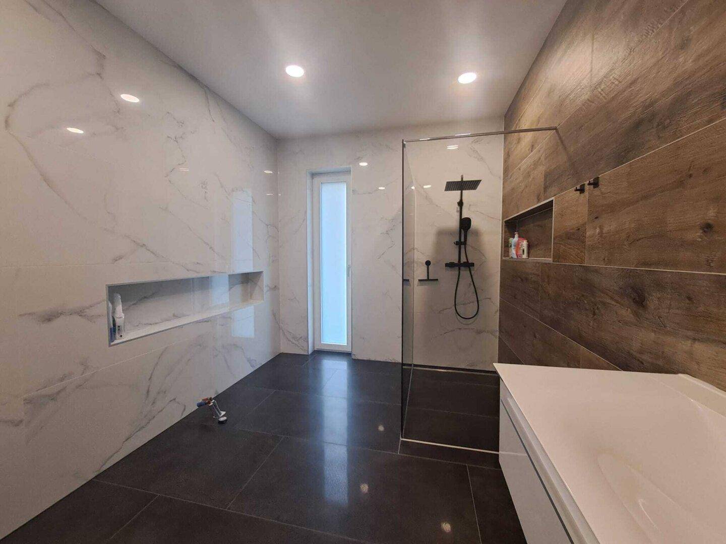 Geräumiges Badezimmer mit begehbarer Dusche, modernen Fliesen und einem Fenster für natürliches Licht.