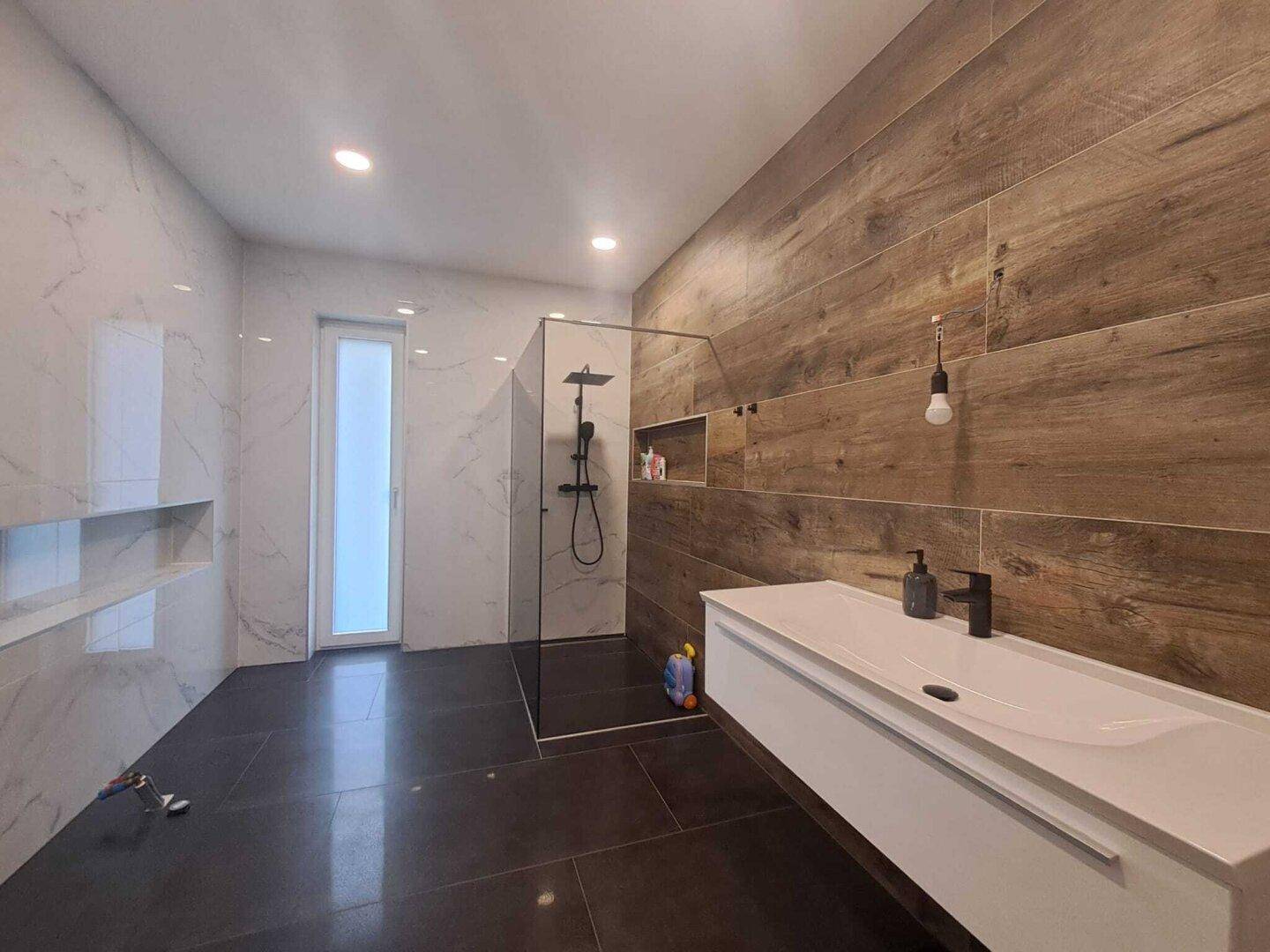 Modernes Badezimmer mit begehbarer Dusche, Holzoptik-Fliesen und eleganten Marmorwänden.