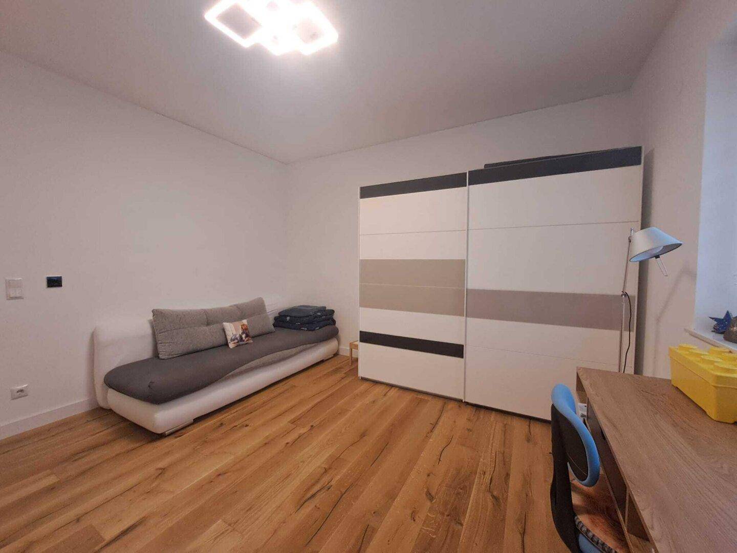 Schlafzimmer mit Holzboden, modernem Kleiderschrank und einem bequemen Tagesbett.