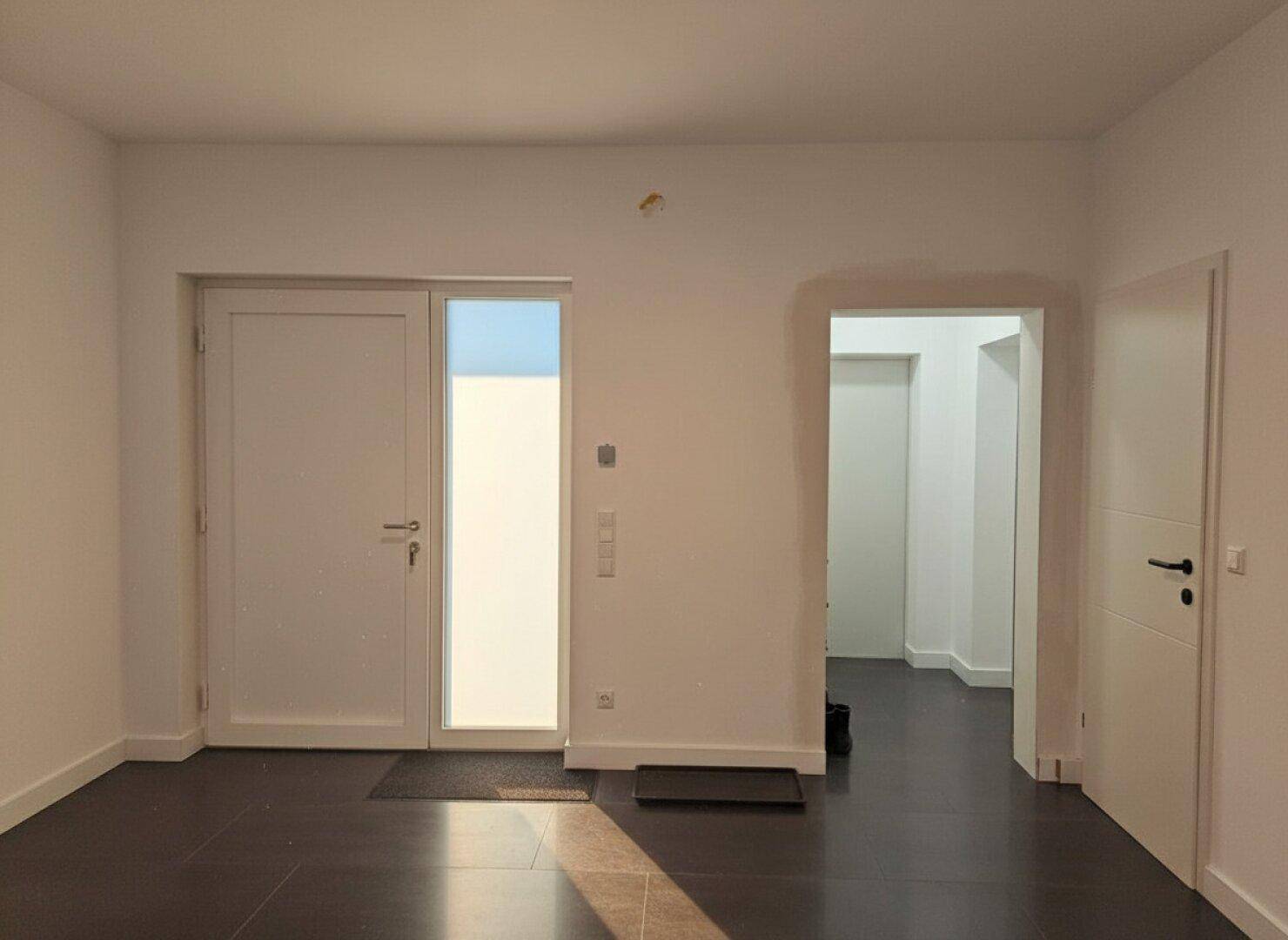 Eingangsbereich mit dunklem Fliesenboden und Zugang zu weiteren hellen Räumen.