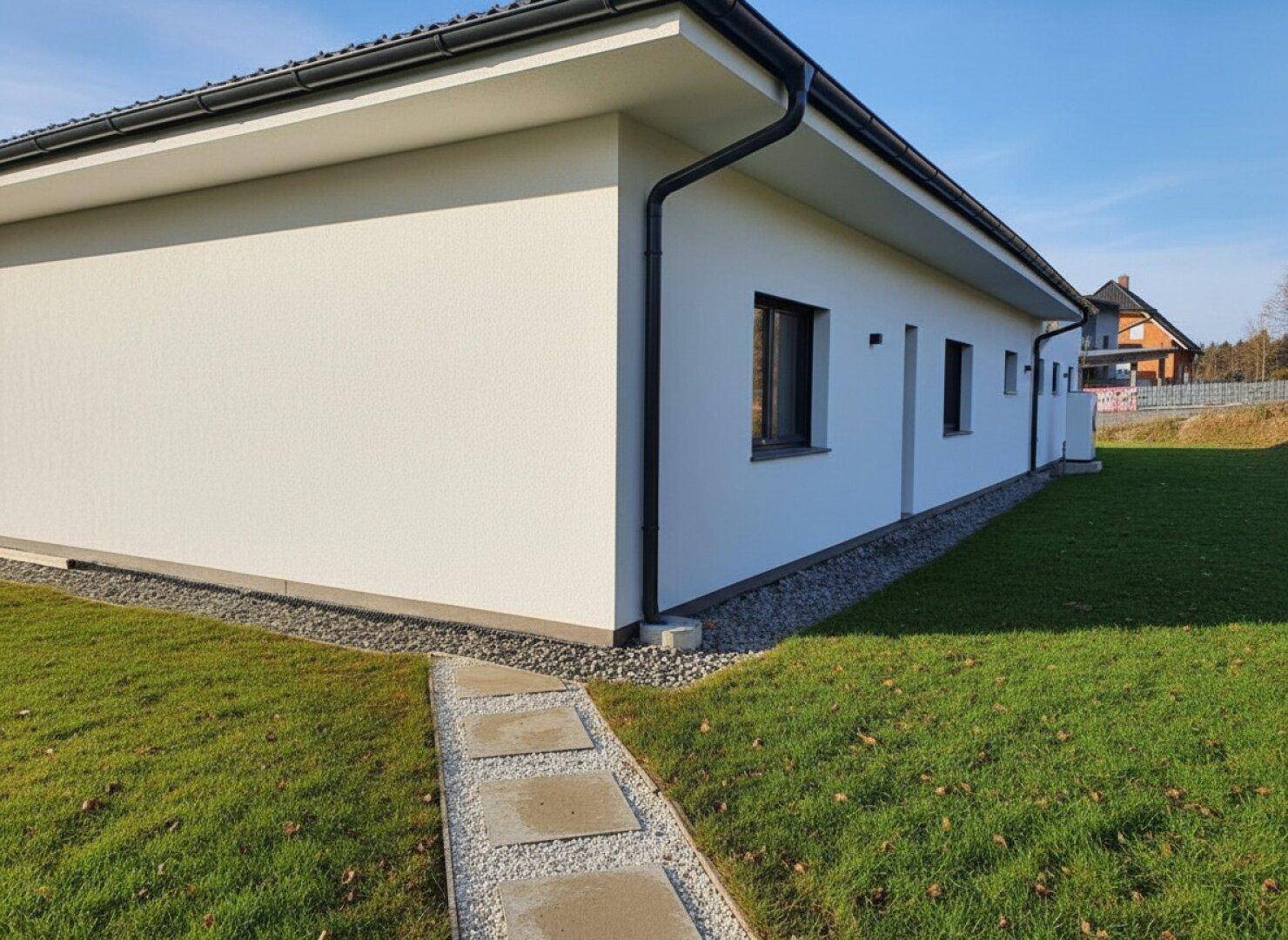 Seitenansicht des modernen Hauses mit gepflegtem Rasen und einem schmalen Gehweg.