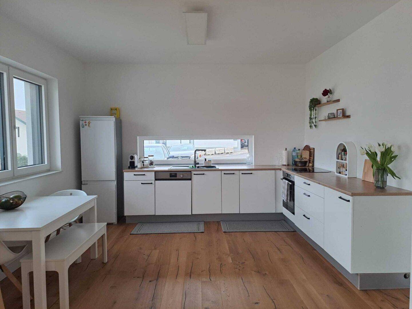 Moderne Einbauküche mit weißen Schränken, Holzarbeitsplatte und integriertem Essbereich.