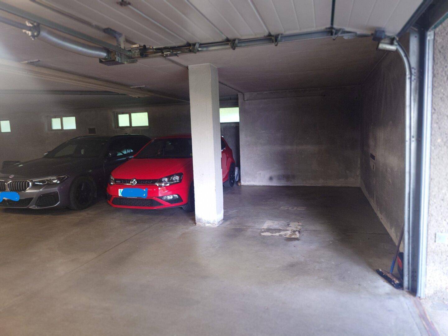 Tiefgarage mit mehreren geparkten Fahrzeugen und sichtbarem Garagentor-Mechanismus.