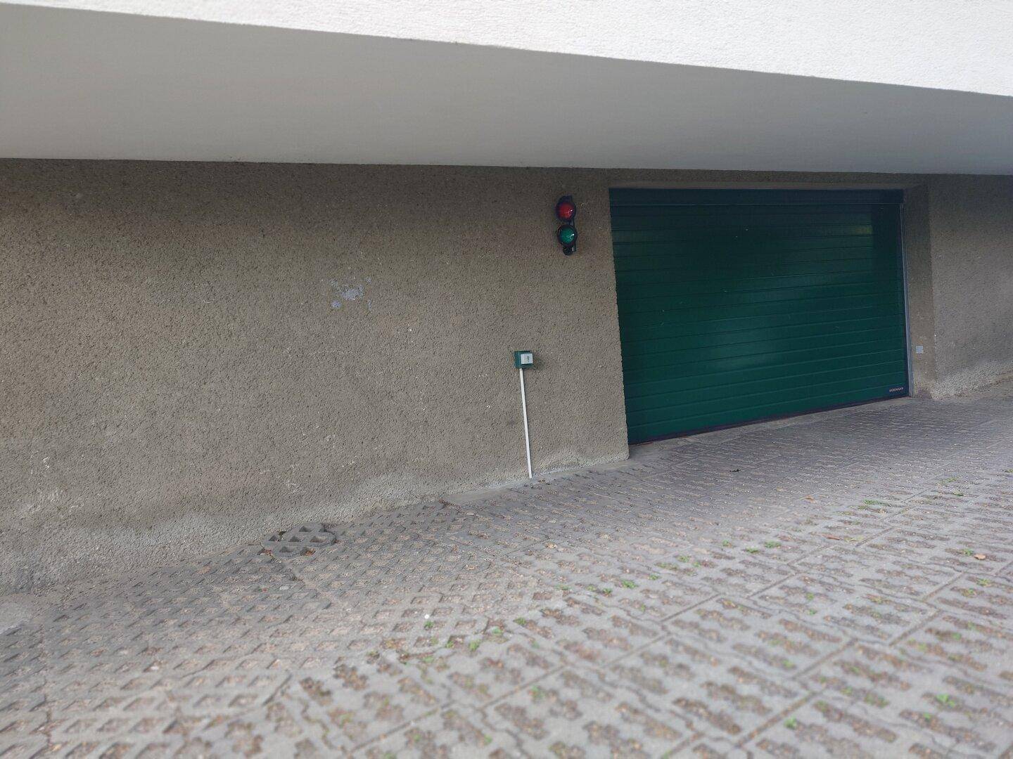 Eingang zur Tiefgarage mit grünem Rolltor, Verkehrsampel und Sensor an der strukturierten Betonwand.