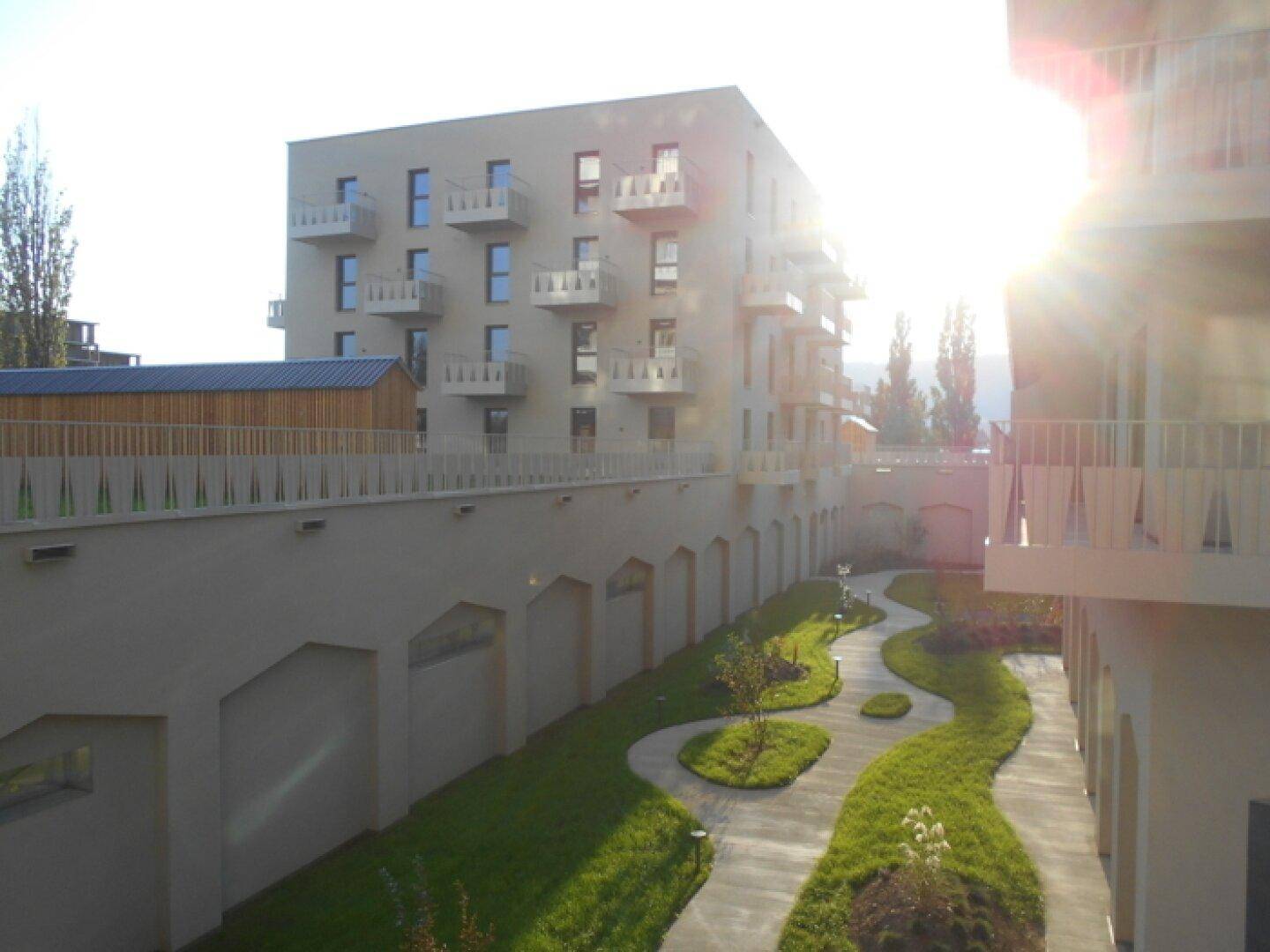 Moderne Wohnanlage mit mehreren Balkonen und einem gepflegten Innenhofgarten mit geschwungenen Wegen.
