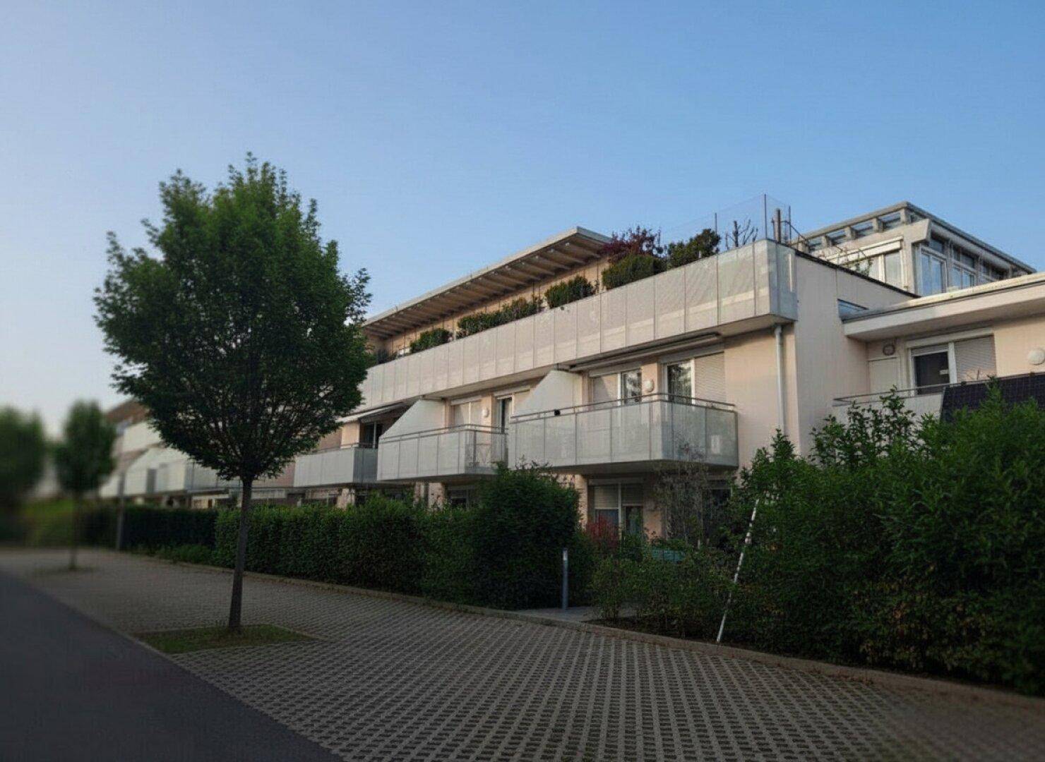 Ansicht eines zeitgenössischen Wohngebäudes mit mehreren Balkonen und einer grünen Hecke.