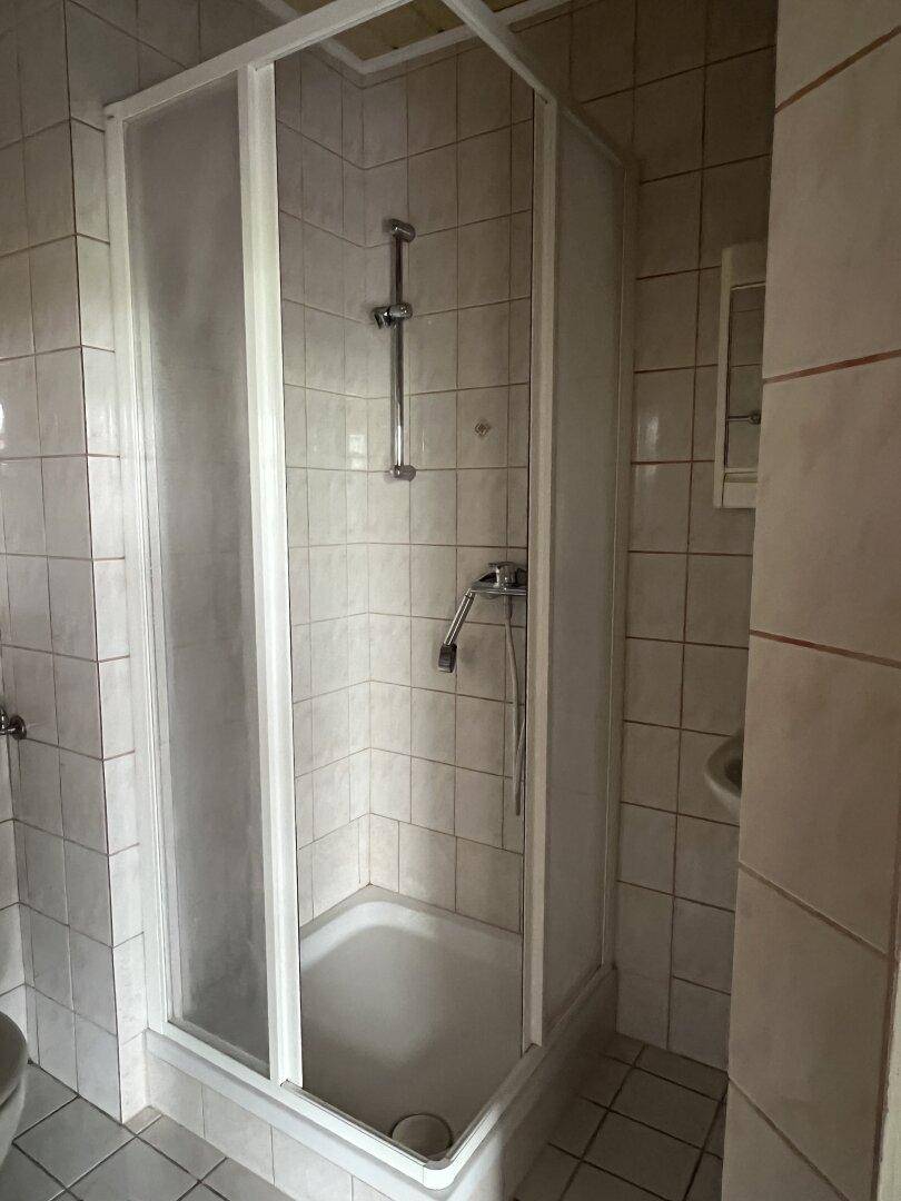 Badezimmer mit Duschkabine und hellen Fliesen an Wänden und Boden.