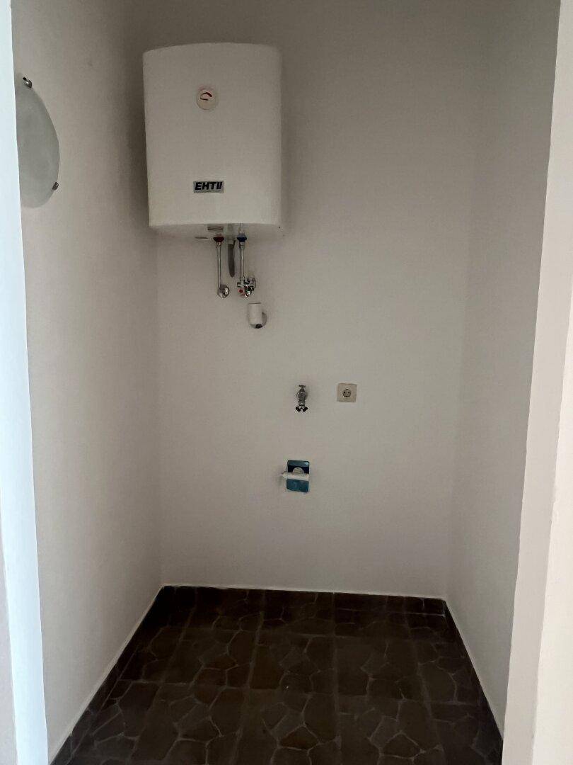 Kleiner Hauswirtschaftsraum mit Warmwasserboiler und dunklem Fliesenboden.