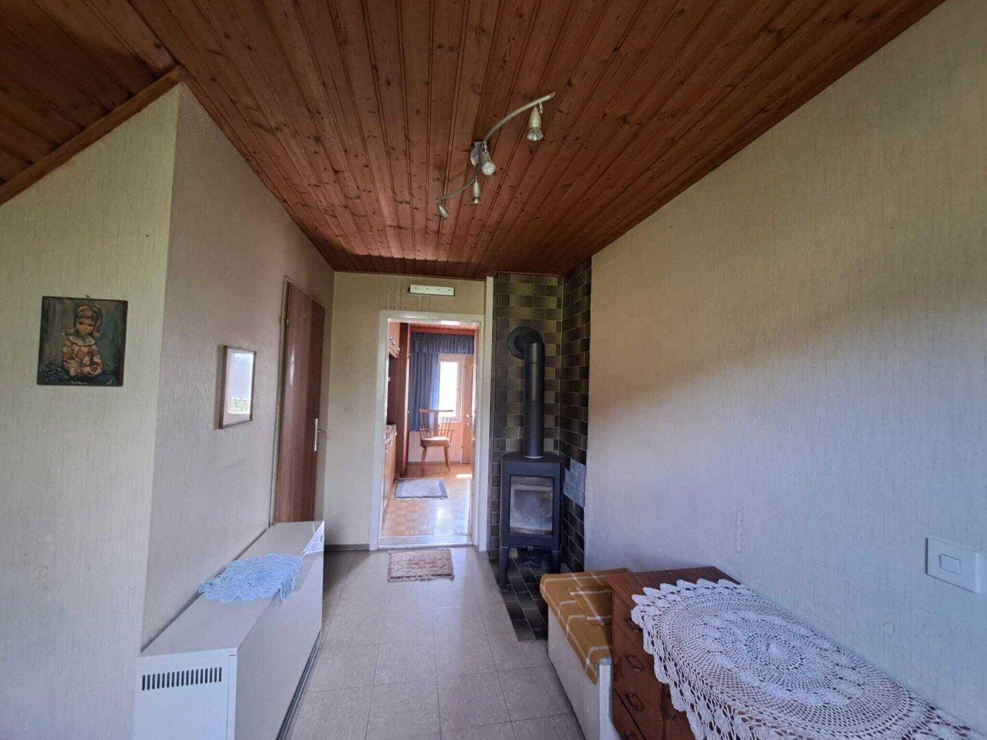 Flur mit Holzdecke, Kaminofen und gefliestem Boden, der zu anderen Räumen führt.