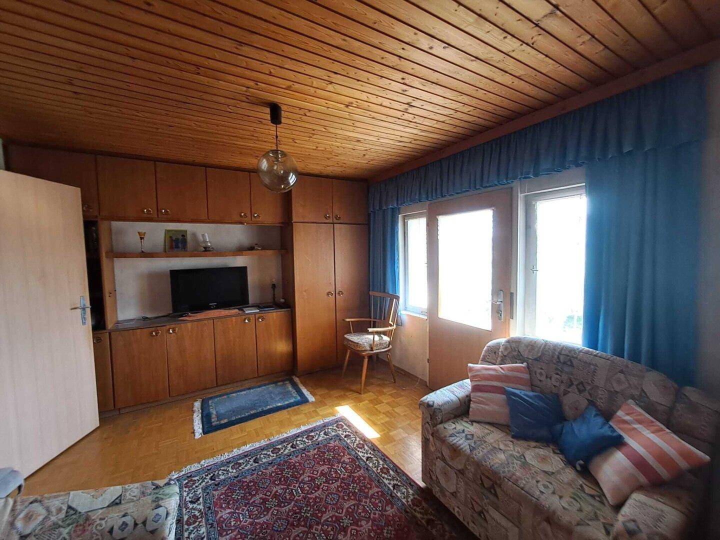Gemütliches Wohnzimmer mit Holzdecke, Einbauschränken und Zugang zum Außenbereich.