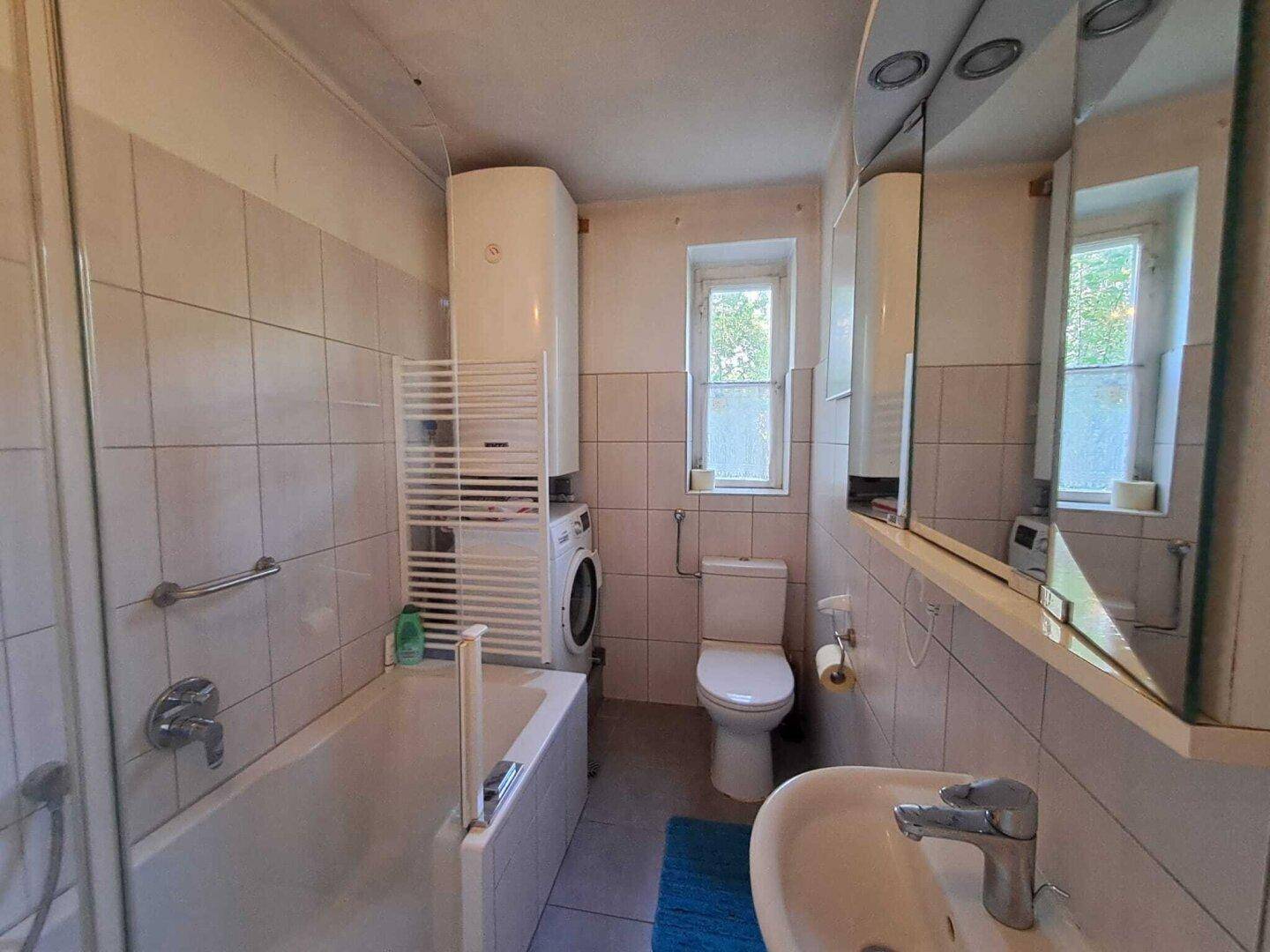 Gefliestes Badezimmer mit Badewanne, WC, Waschbecken und Fenster.