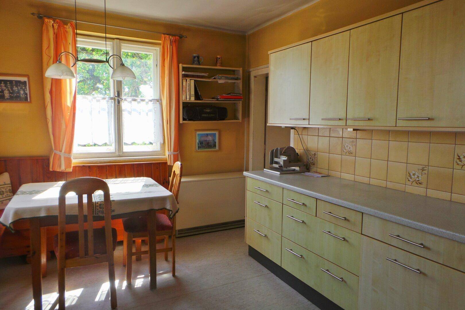 Helle Küche mit hellen Holzschränken, gelben Fliesen und Essbereich am Fenster.