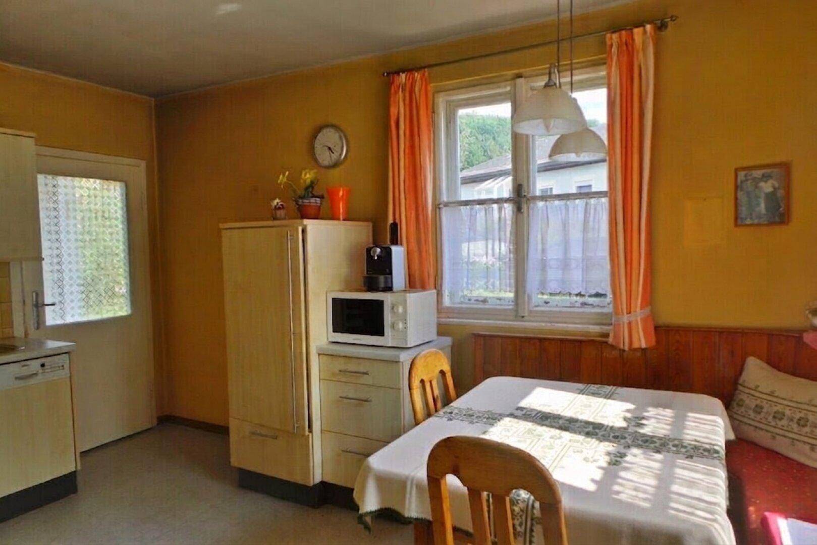 Gemütliche Küche mit Essbereich, gelben Wänden und Blick ins Grüne durch das Fenster.
