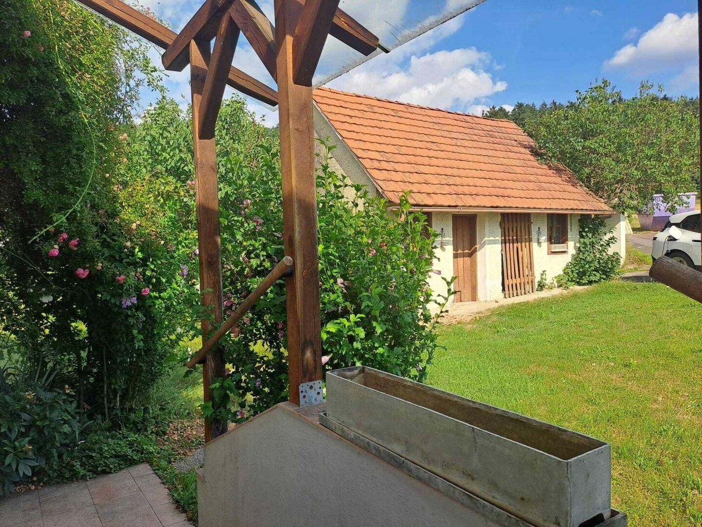 Kleines Nebengebäude mit rotem Ziegeldach umgeben von üppigem Grün im Garten.