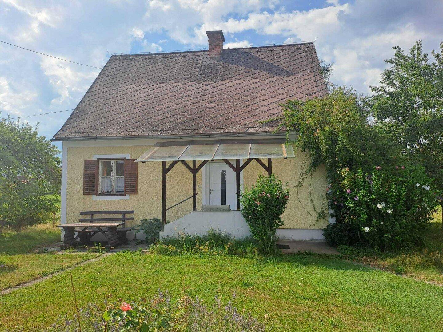 Charmantes gelbes Landhaus mit rotem Dach, überdachtem Eingang und Vorgarten.