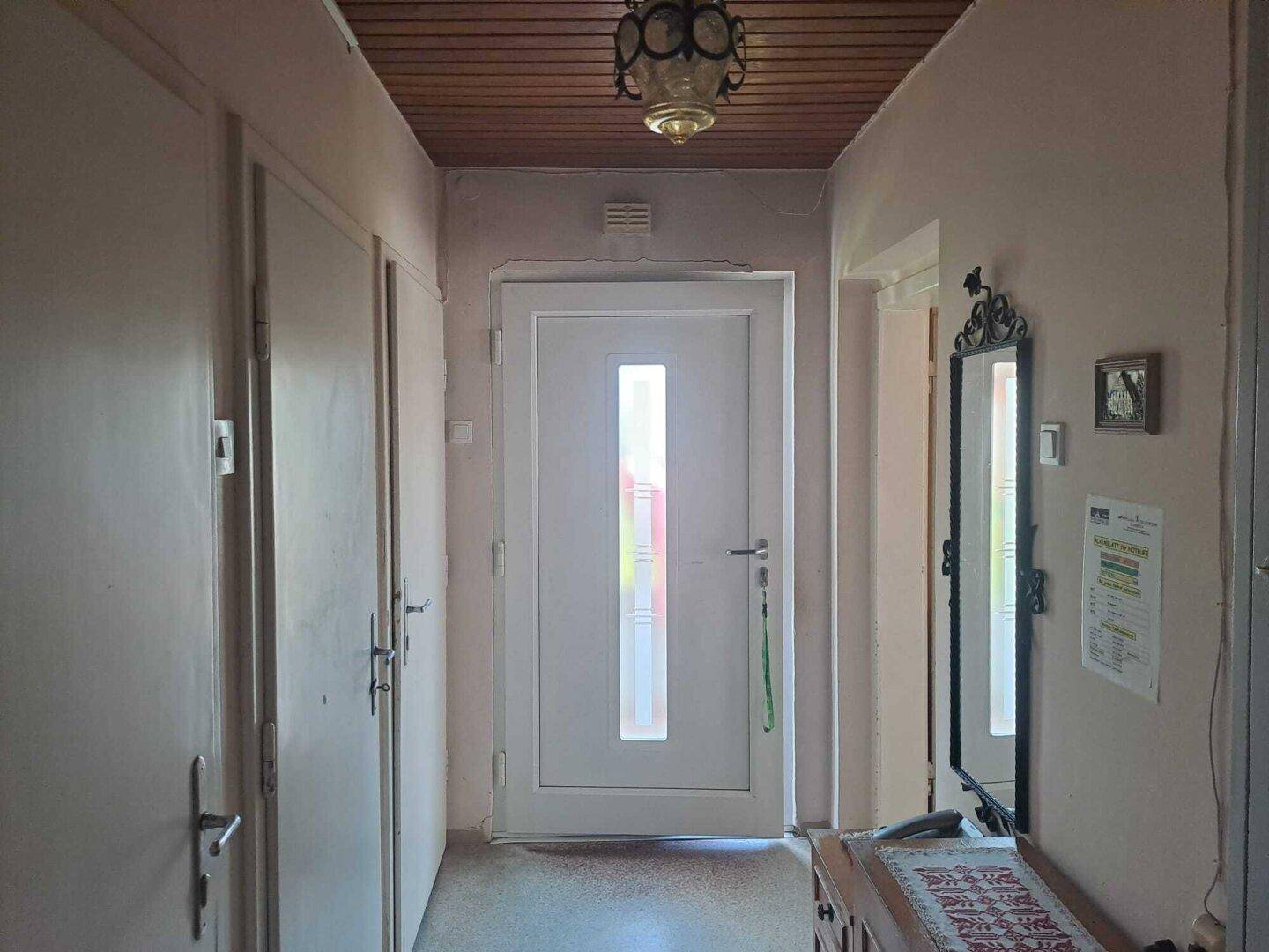 Heller Flur mit Holztäfelung an der Decke und einer modernen Eingangstür.