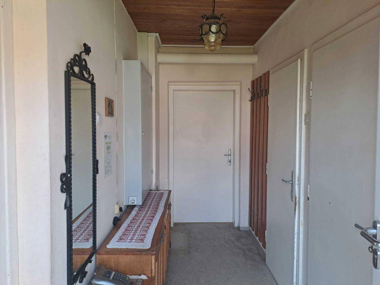 Schmaler Flur mit Holzdecke, Spiegel und Garderobe, der zu weiteren Räumen führt.