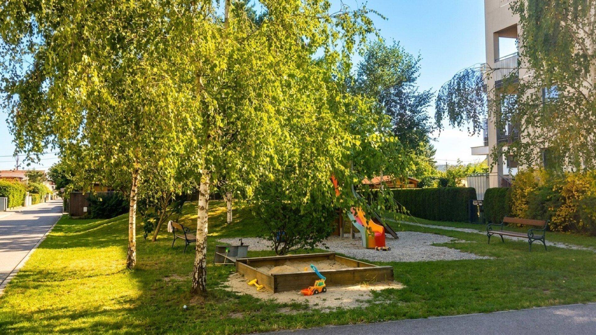 Detailansicht des Spielplatzes mit Sandkasten und Rutsche im grünen Außenbereich der Wohnanlage.