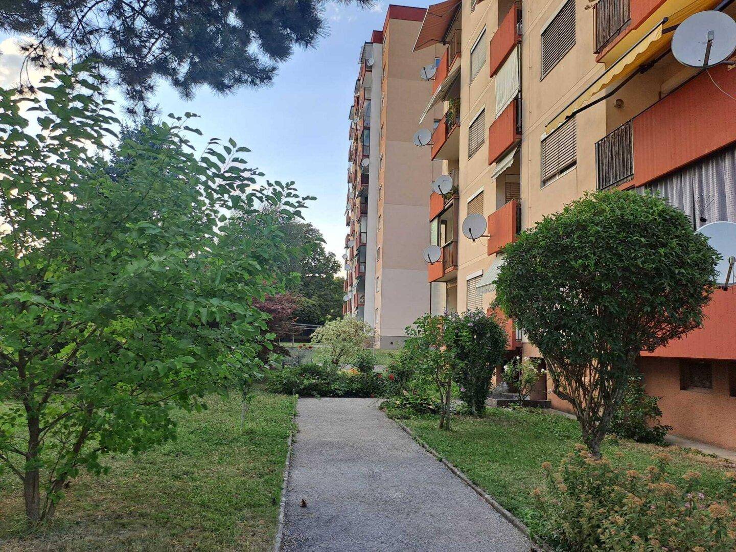 Seitenansicht eines Mehrfamilienhauses mit Balkonen und einem gepflegten Grünbereich mit Gehweg.