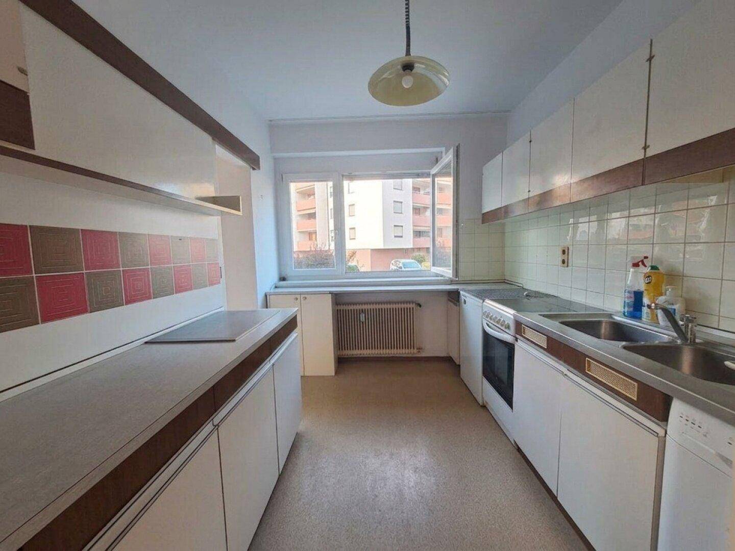 Funktionale Küche im Vintage-Stil mit Einbauschränken, Spüle und Fenster mit Blick nach draußen.