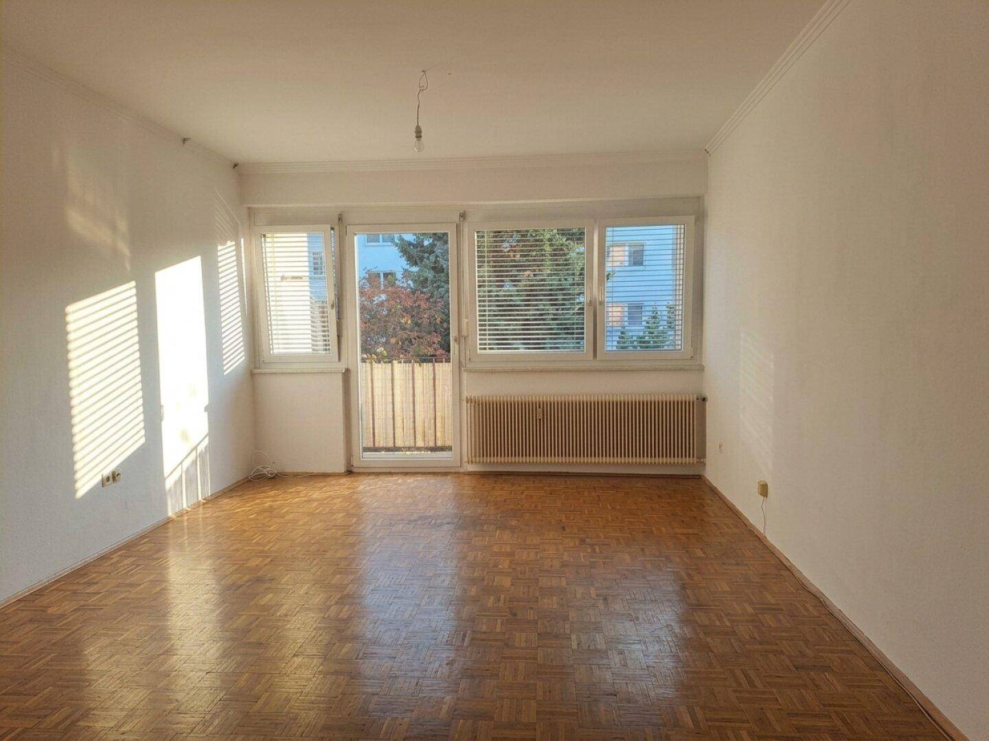 Helles Wohnzimmer mit Fischgrätparkettboden, großen Fenstern und Zugang zum Balkon.