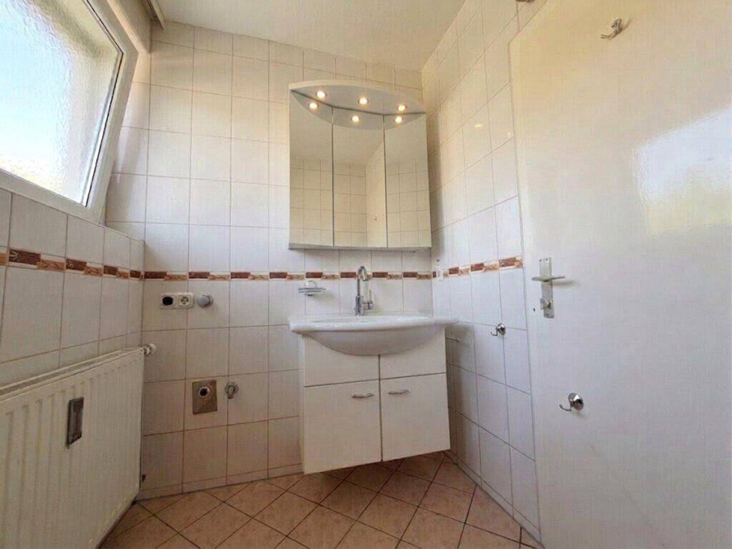 Helles Badezimmer mit Fliesen, Waschbecken und Spiegelschrank, bereit für die Installation einer Dusche.