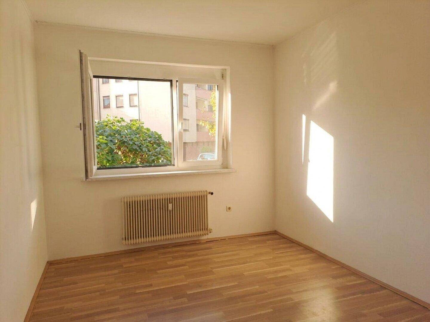 Helles Schlafzimmer mit Parkettboden und einem Fenster, das viel natürliches Licht hereinlässt.