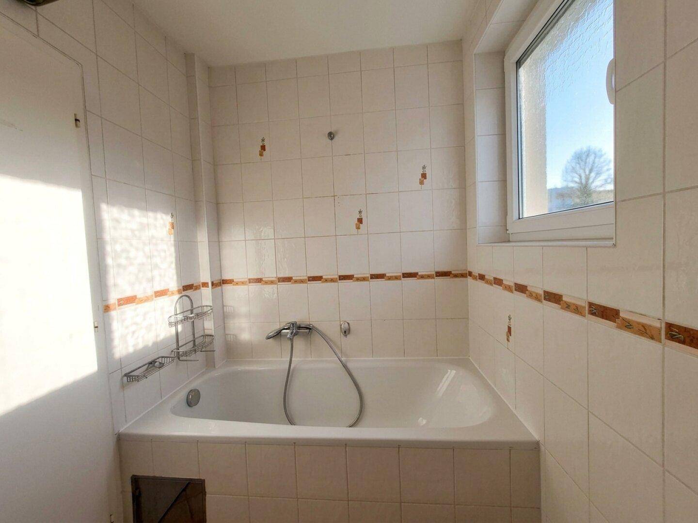Badezimmer mit Badewanne, Fliesen und Fenster, das für natürliche Belüftung und Licht sorgt.
