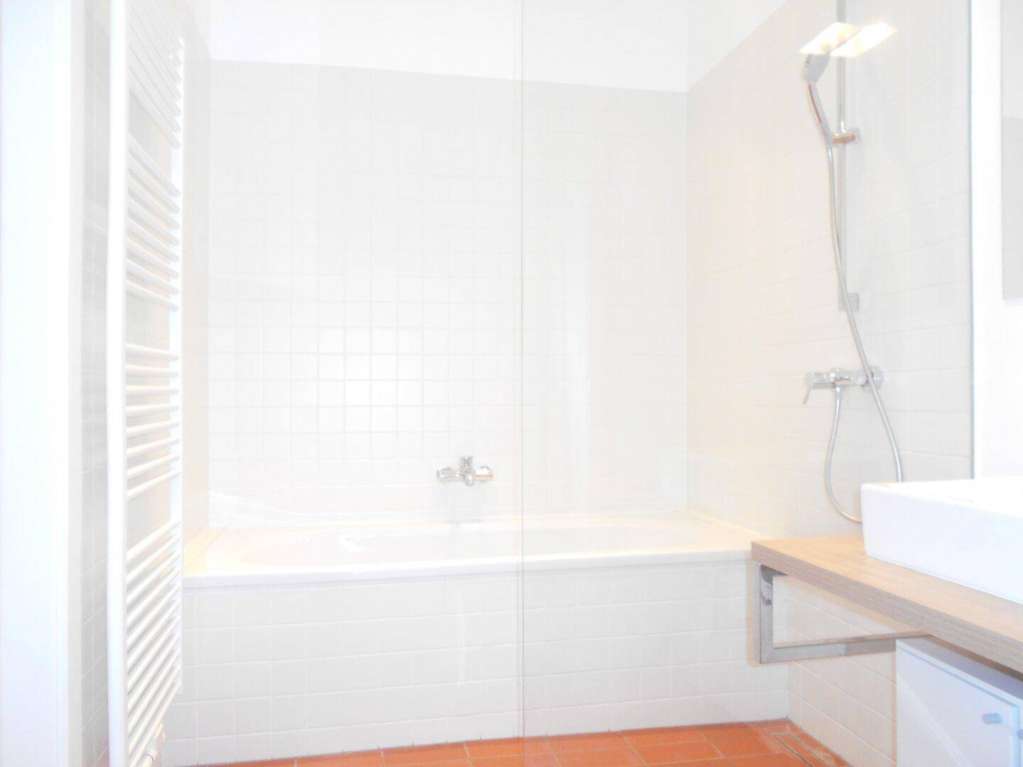 Helles Badezimmer mit Badewanne, Duscharmatur und weißem Handtuchheizkörper auf Terrakotta-Fliesen.