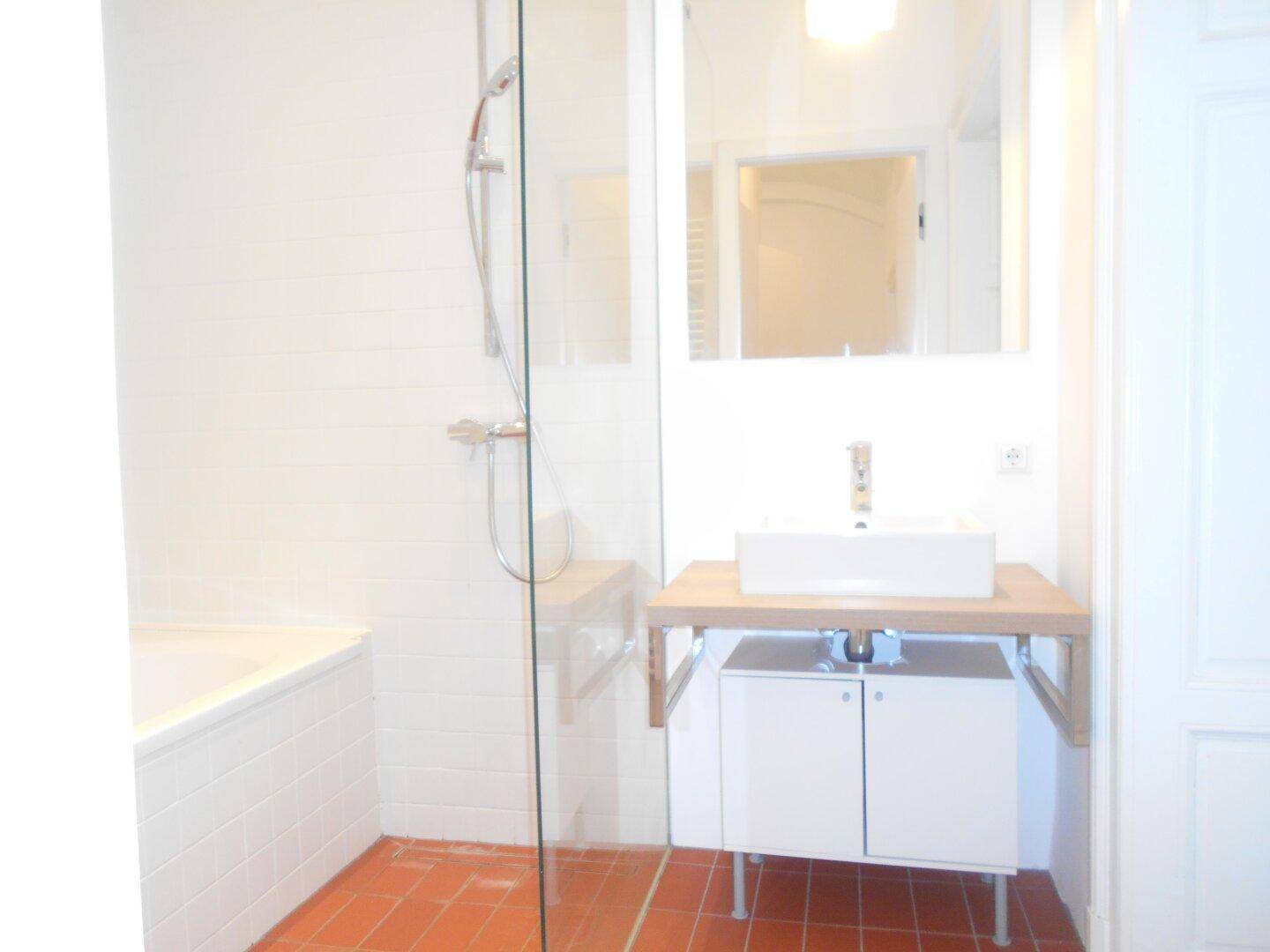 Modernes Badezimmer mit weißem Waschbecken auf Holzplatte, Dusche und Badewanne sowie Terrakotta-Fliesen.