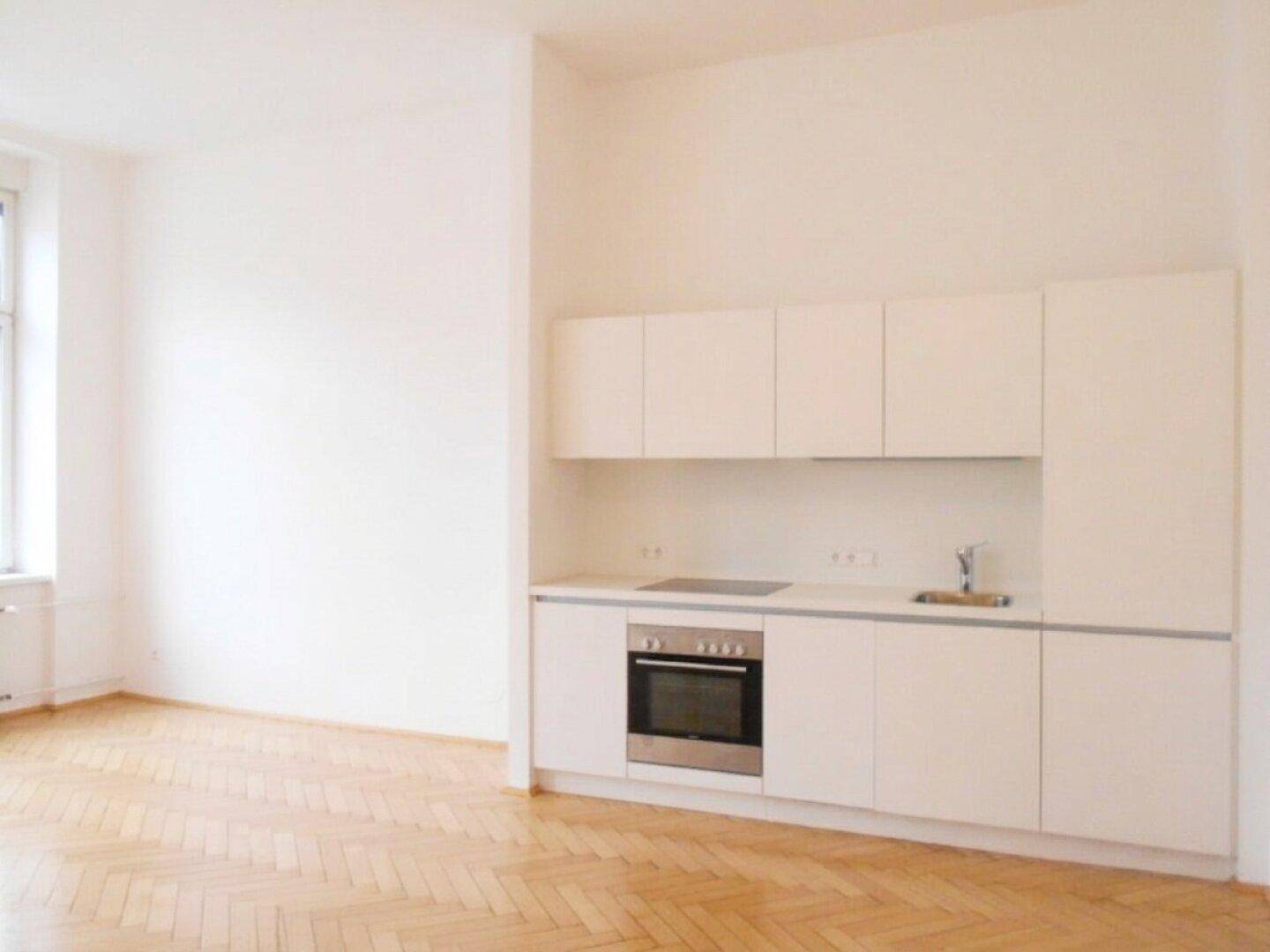 Moderne Küchenzeile mit weißen Fronten, integriertem Kochfeld und Backofen, kombiniert mit hellem Parkettboden.