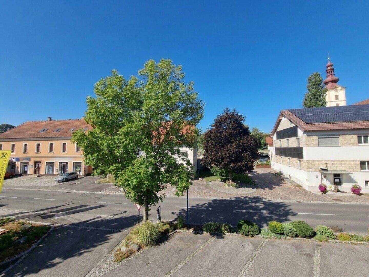 Blick auf eine belebte Straße mit Gebäuden, Bäumen und einem Kirchturm im Hintergrund.