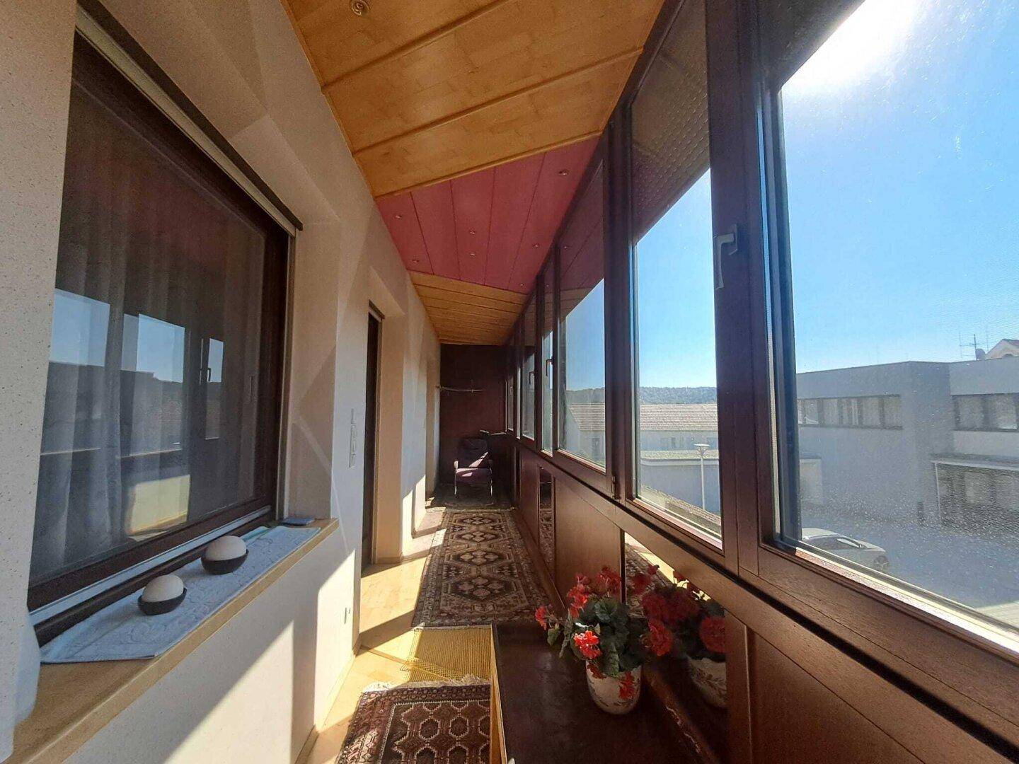 Verglaste Loggia mit Holzboden und weitem Blick, ideal als sonniger Rückzugsort.