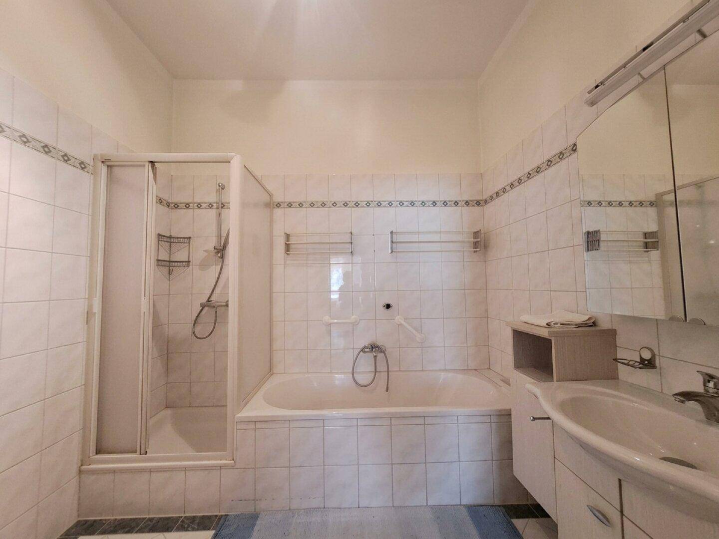 Badezimmer mit Badewanne und integrierter Dusche, Waschtisch und hellen Fliesen.