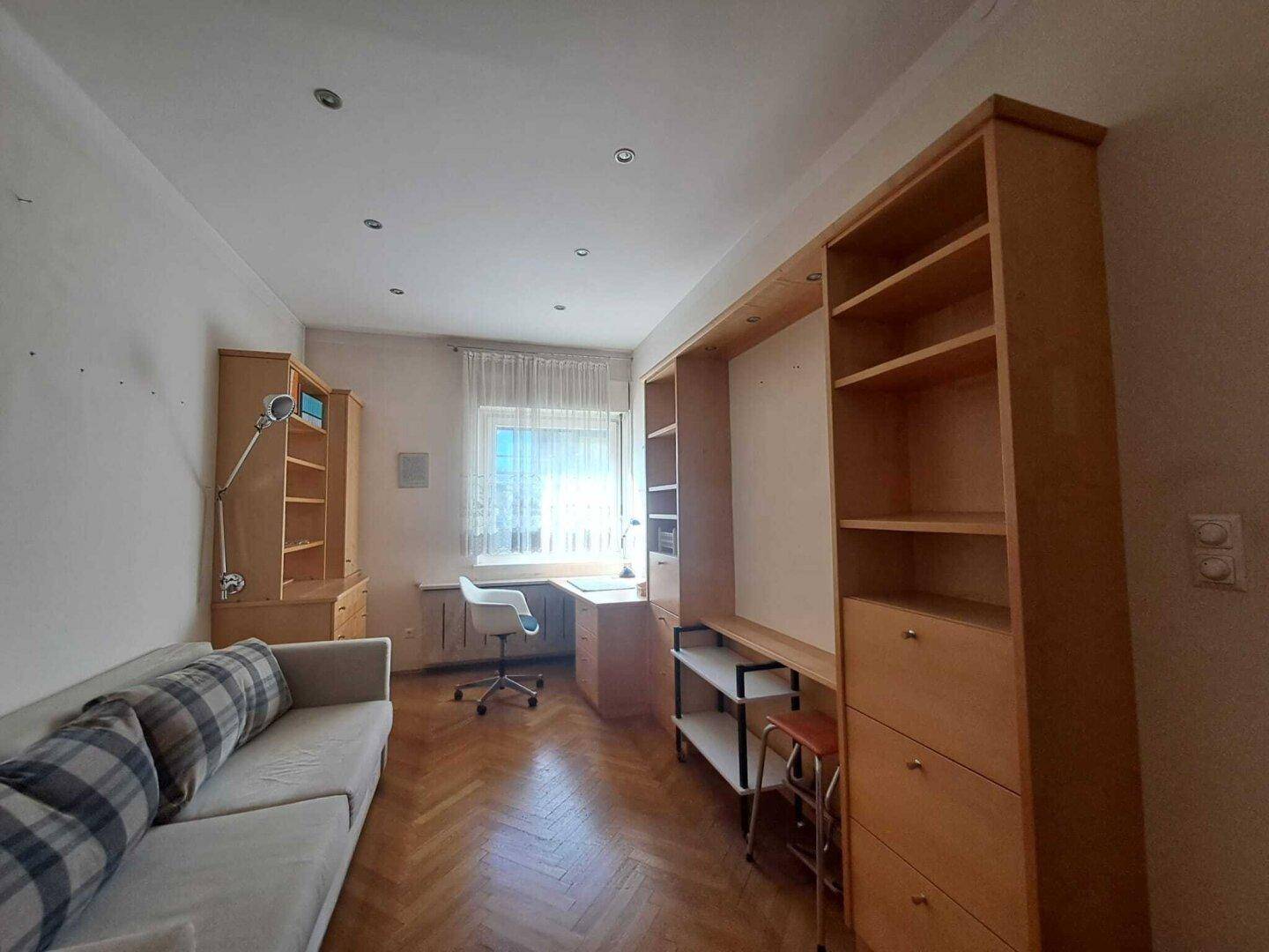 Helles Schlafzimmer mit Parkettboden, Schreibtisch und Einbauregalen, ideal als Kinder- oder Arbeitszimmer.